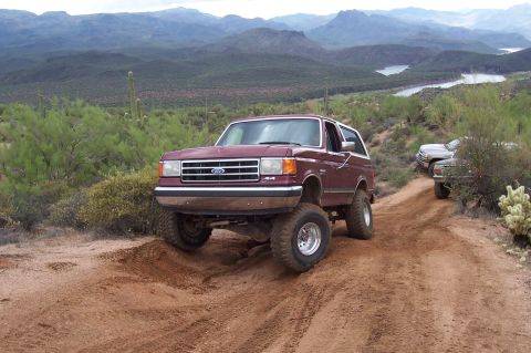 1992 Ford Bronco - A maroon Ford Bronco navigates a dusty trail with other vehicles in the background.