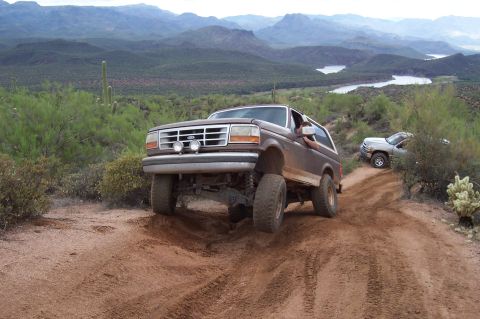 1992 Ford Bronco - A 1992 Ford Bronco navigates a steep, dusty trail in a mountainous desert landscape.