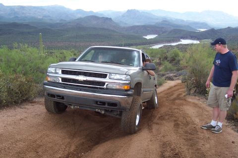 1992 Ford Bronco - A silver Chevrolet pickup truck navigates a dusty trail with a scenic mountain backdrop and a man standing nearby.