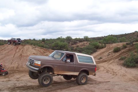 1992 Ford Bronco - A 1992 Ford Bronco navigates a dusty off-road course with another vehicle visible on a distant hill.