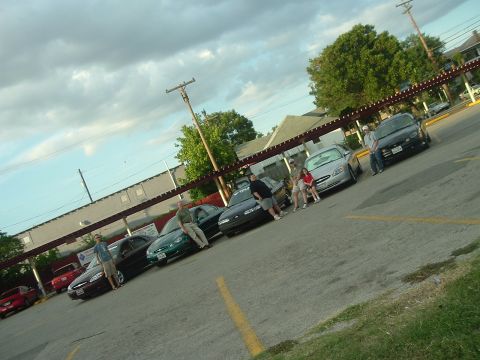 1993 Ford Taurus - A group of people gather around several cars in a parking lot on a cloudy day.