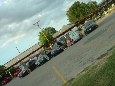 1993 Ford Taurus - A group of people gathered around several parked cars in a parking lot.