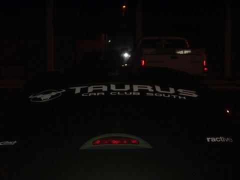 1993 Ford Taurus - A car with a club decal is parked at night, with a truck in the background.