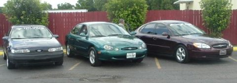 1993 Ford Taurus - Three Ford Taurus sedans are parked side-by-side in a lot, displaying different colors and model years.