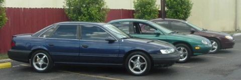 1993 Ford Taurus - A blue 1993 Ford Taurus sedan is the lead vehicle in a line of three cars parked outdoors.