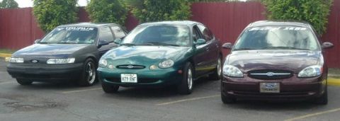 1993 Ford Taurus - Three Ford Taurus sedans are parked in a lot, with two dark colored and one green visible.