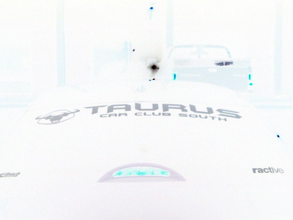Taurus Car Club South logo on a white car hood, with a pickup truck visible in the background