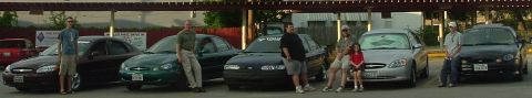 1993 Ford Taurus - A group of people pose with several Ford Taurus sedans parked in a lot.