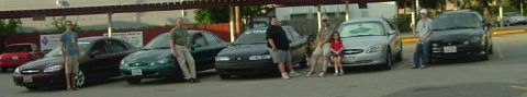 1993 Ford Taurus - Several Ford Taurus sedans are parked in a lot with people standing around them.