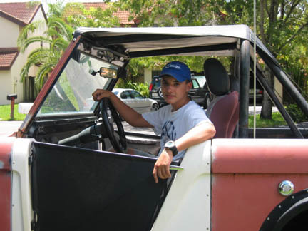 1972 Ford Bronco - A young person sits in the driver's seat of a red and white 1972 Ford Bronco, with another vehicle visible in the background.