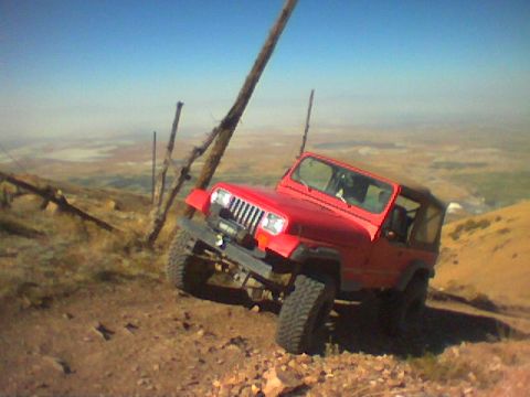 1979 Ford Bronco - A red Jeep Wrangler navigates a steep, rocky incline under a clear blue sky.