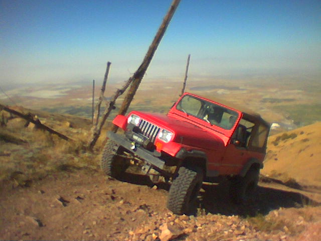 Red Jeep Wrangler on a dirt hill, leaning to the side