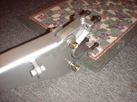 1988 Ford Bronco - Close-up of the axle end of a silver-painted fabricated radius arm on carpet, showing the boxed plate arm, a welded reinforcing rib, twin m…
