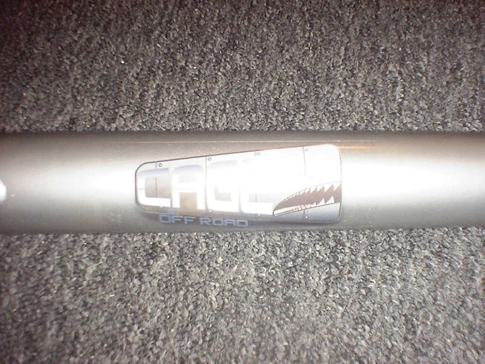 Silver roll bar tube with a 'Cage Off Road' shark-mouth decal on gray carpet