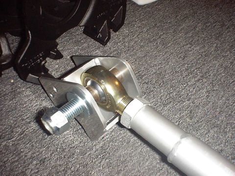1988 Ford Bronco - Detail of a gold cadmium-plated heim/rod end threaded into a silver tube link and locked with a jam nut, captured between the tabs of a bar…