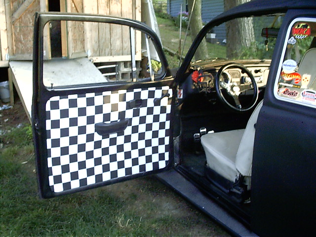 Dark VW Beetle with open driver door showing black and white checkered custom door panel and tan interior