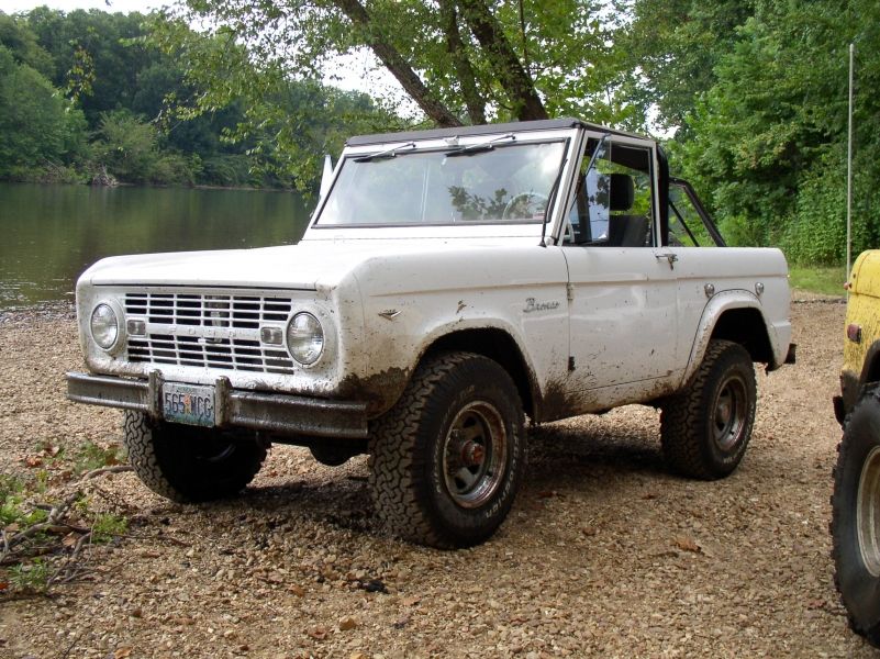 White 1967 Ford Bronco parked by a river, with another vehicle partially visible on the right