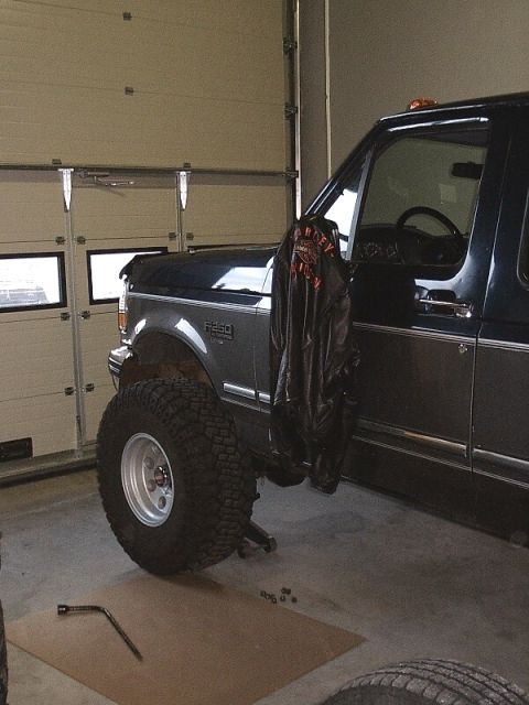 1996 Ford Bronco - Ford F-250 truck undergoing modification in a garage, showing lifted suspension and large off-road tires.