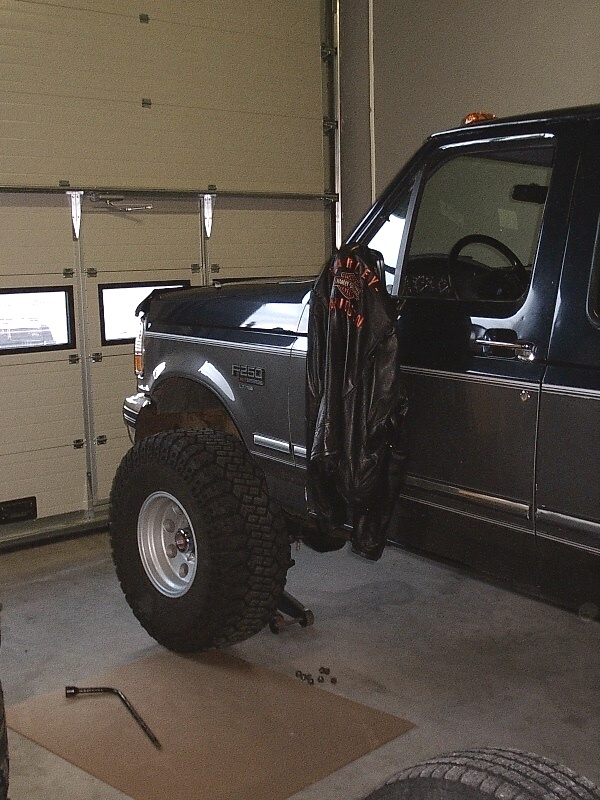 Dark blue lifted Ford on jack stand in garage, wheel off, tools on floor