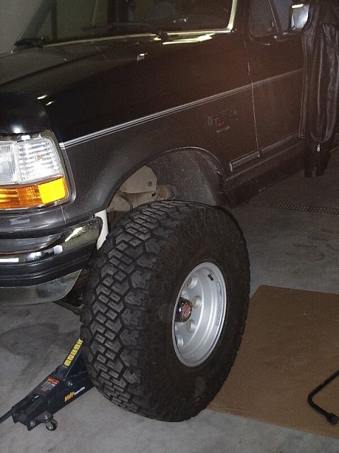 1996 Ford Bronco - A black Ford Bronco is shown with its front passenger side tire being changed.