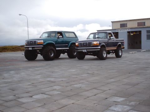 1996 Ford Bronco - Two modified Ford trucks, a Bronco and a pickup, are parked side-by-side on a paved lot.
