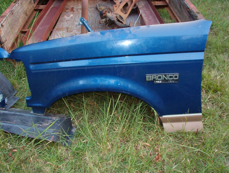 Blue Ford Bronco left front fender with chrome emblem lying on grass