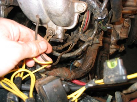 1986 Ford F-150 - Close-up of a hand manipulating wires within a vehicle's engine compartment.