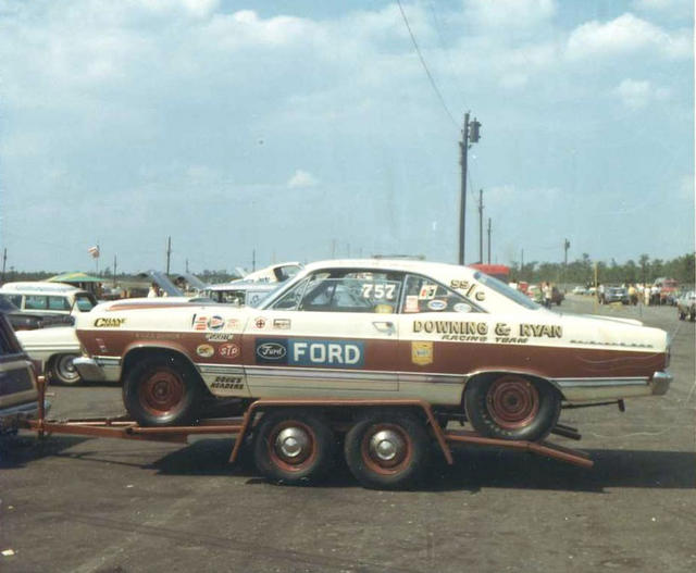 Vintage white and maroon Ford drag racing coupe on a trailer at a track