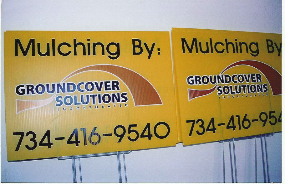 Two yellow signs advertising "Mulching By Groundcover Solutions" with phone number 734-416-9540