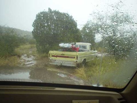 1989 Ford Bronco - Ford pickup truck navigating muddy conditions, viewed from inside another vehicle through a wet windshield.