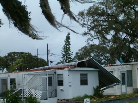 1979 Ford Bronco - A mobile home shows significant damage from a storm, with its awning completely collapsed and debris scattered around.