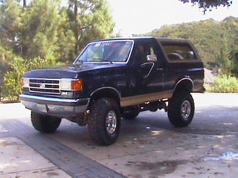 1991 Ford Bronco - Dark blue Ford Bronco full-size SUV with tan lower two-tone bodyside, photographed from the front three-quarter angle on a concrete drivewa…
