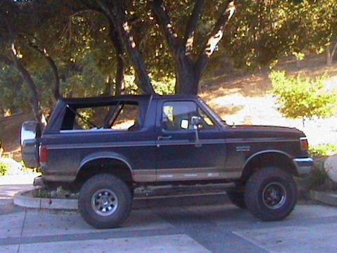 1991 Ford Bronco - Side view of a 1991 Ford Bronco, parked on pavement with trees in the background.