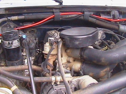 1991 Ford Bronco - Cleaned-up engine bay viewed from the front, showing a black air cleaner or intake cover, a black canister filter mounted on the fender, re…