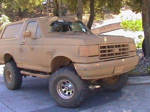 1991 Ford Bronco - Front three-quarter view of a lifted full-size Ford Bronco in a driveway, its body, hardtop, bumper and grille completely covered in dried…