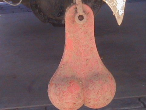 1991 Ford Bronco - Tight close-up of red novelty "truck nutz" hanging from a trailer hitch under a vehicle, caked in dried mud after an off-road run. A muddy…