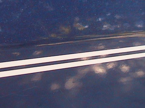 1991 Ford Bronco - Extreme close-up of a freshly applied dual white pinstripe with thin dark outlines running diagonally across a dark blue body panel. Water…