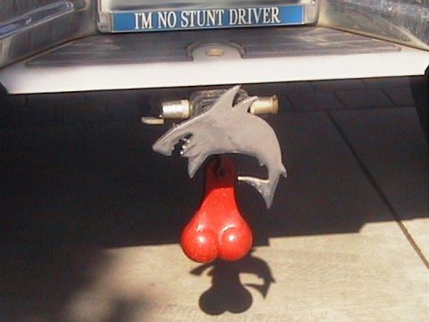 1991 Ford Bronco - Close-up of a chrome receiver hitch on a truck's rear bumper fitted with a novelty shark-shaped hitch cover and red plastic "truck nutz" ha…