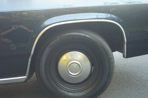 1991 Ford LTD Crown Victoria - A dark-colored vehicle's rear wheel and fender are shown, with chrome trim accenting the wheel well.