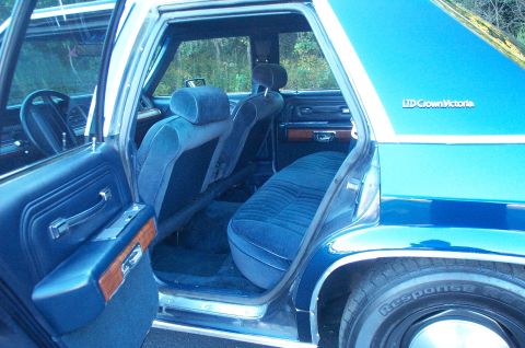 1991 Ford LTD Crown Victoria - Interior shot through the open rear doors of a blue Ford LTD Crown Victoria wagon, showing blue cloth split-bench seating, matching blue do…