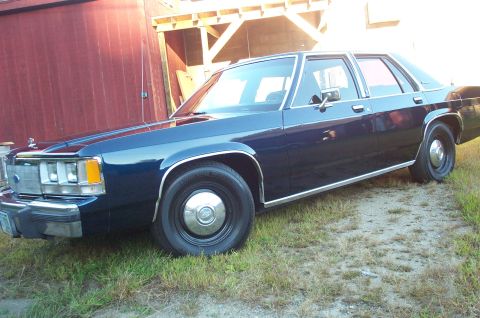 1991 Ford LTD Crown Victoria - Dark blue sedan with chrome trim parked outside a barn.