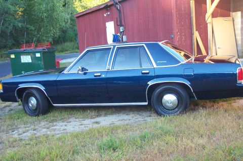 1991 Ford LTD Crown Victoria - A dark blue 1991 Ford Crown Victoria LTD sedan is parked outdoors next to a red building.