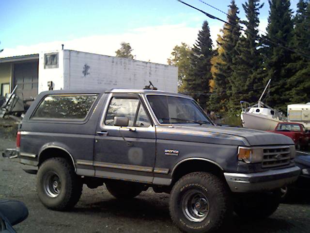 Two-tone gray lifted Ford Bronco on BFGoodrich tires parked in a gravel yard with boat behind