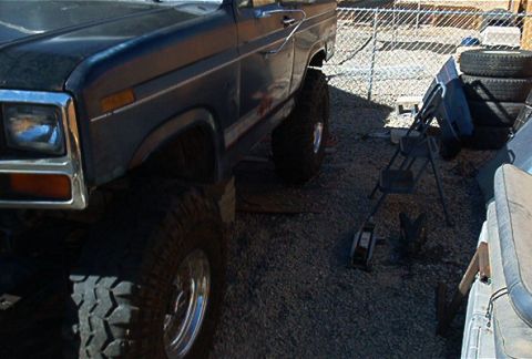 1986 Ford Bronco - This lifted Ford Bronco is parked outdoors on a gravel surface, with a fence and stacked tires in the background.