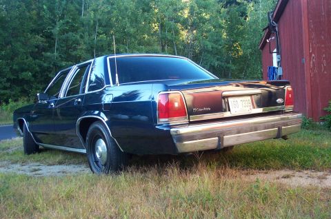 1991 Ford LTD Crown Victoria - Rear view of a dark blue 1991 Ford Crown Victoria LTD sedan parked next to a red building.