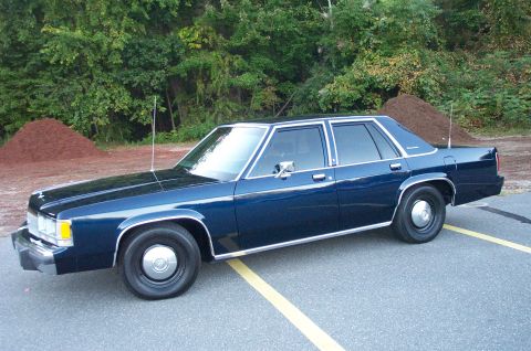 1991 Ford LTD Crown Victoria - Driver's-side profile of a dark blue boxy Ford LTD Crown Victoria four-door sedan on black steel wheels with chrome center caps, with twin…