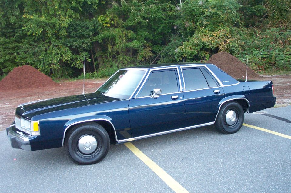 Dark blue boxy Ford LTD Crown Victoria sedan with whip antennas, side view