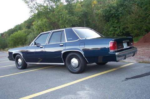 1991 Ford LTD Crown Victoria - Rear three-quarter view of a dark blue boxy Ford LTD Crown Victoria four-door sedan on black steel wheels with chrome center caps, with an…