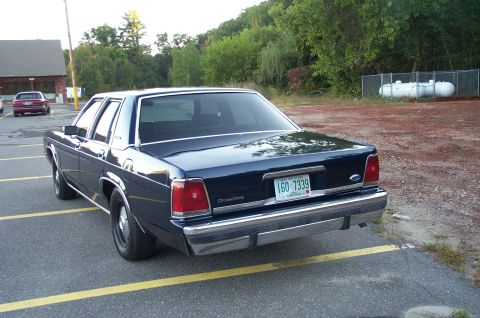 1991 Ford LTD Crown Victoria - A dark blue sedan is parked in a lot, with another car visible in the background.