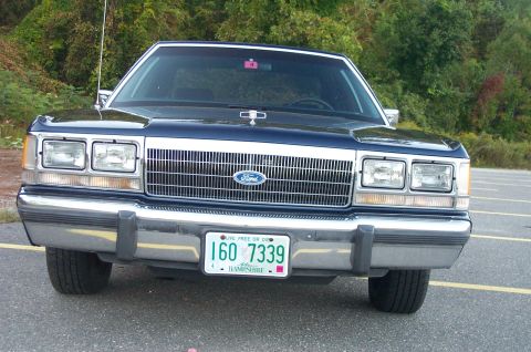 1991 Ford LTD Crown Victoria - The front of a 1991 Ford Crown Victoria is shown parked in an outdoor lot with trees in the background.